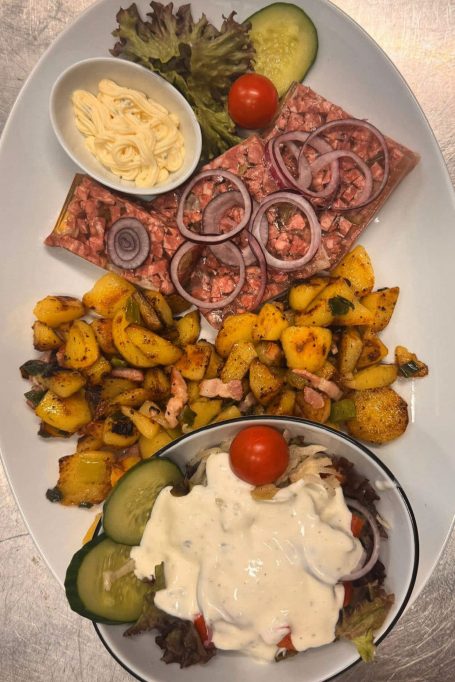 Sülze mit Bratkartoffeln Verschiedene Salate mit Gemüse, einer Tomate, Zwiebeln und einer Beilage aus Käse.