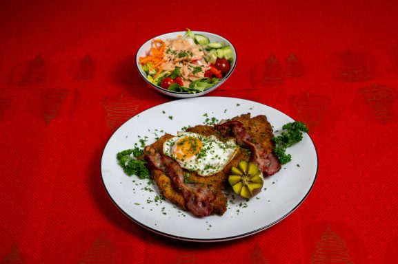 Gegrilltes Fleisch mit Spiegelei, garnierter Salat und einer Limette auf einem roten Tisch.